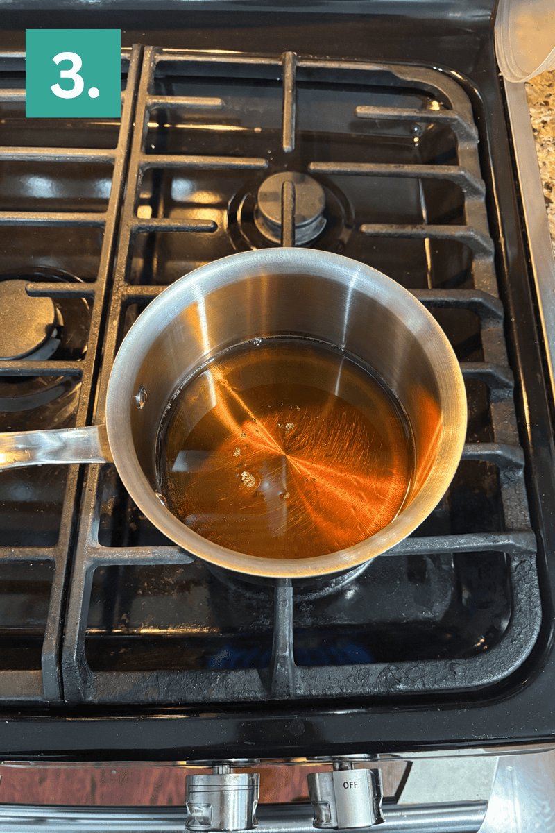 A stainless steel saucepan with caramel-colored liquid is heating on a gas stove. A green box with the number 3 is in the top left corner of the image.