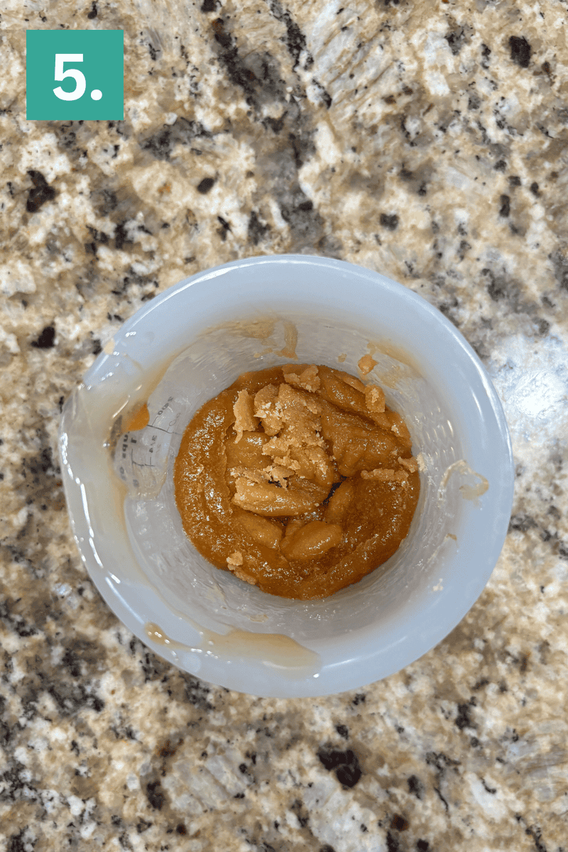 A white mixing bowl on a granite countertop contains an orange-brown paste with crumbly chunks. A green box with the number 5 is in the top left corner of the image.