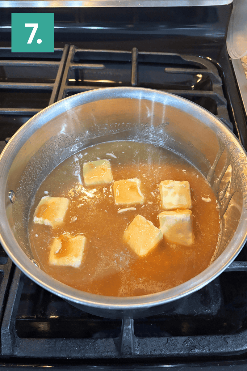 A saucepan with caramel sauce and six cubes of butter melting on a stovetop burner. A green box with the number 7 is in the top left corner of the image.
