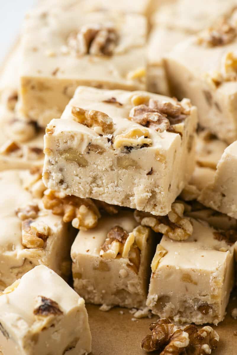 Close-up of creamy maple walnut fudge squares, stacked and topped with walnut pieces, displaying a smooth texture and nutty filling.