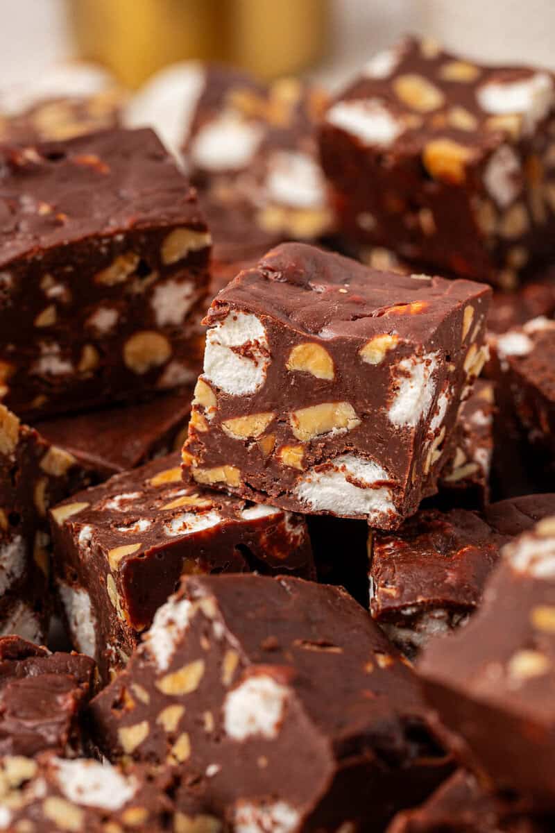 A close-up of chocolate fudge squares with visible chunks of nuts and marshmallows, stacked on top of each other.