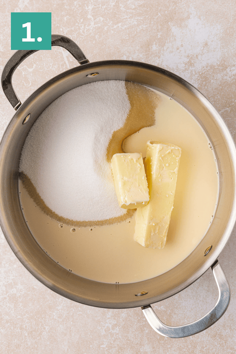 A metal pot containing two sticks of butter, granulated sugar, a brown liquid (possibly vanilla), and a creamy liquid, viewed from above. A green box labeled 1. is in the top left corner of the image.