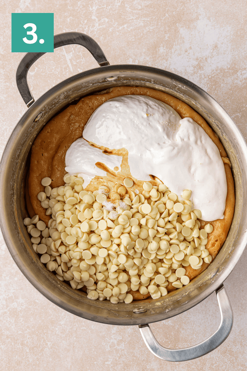 A saucepan filled with cookie dough mixture, topped with white chocolate chips and a dollop of marshmallow cream. A green box with the number 3 appears in the top left corner.