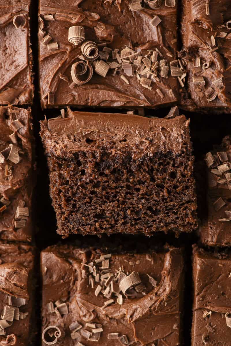 Close-up of chocolate cake squares topped with creamy chocolate frosting and chocolate shavings, with one piece slightly raised above the others.