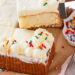 A rectangular white cake with white frosting and colorful sprinkles is cut into squares. A spatula lifts one piece, showing a fluffy texture. Text reads 9x13 inch cake - The Best White Cake.