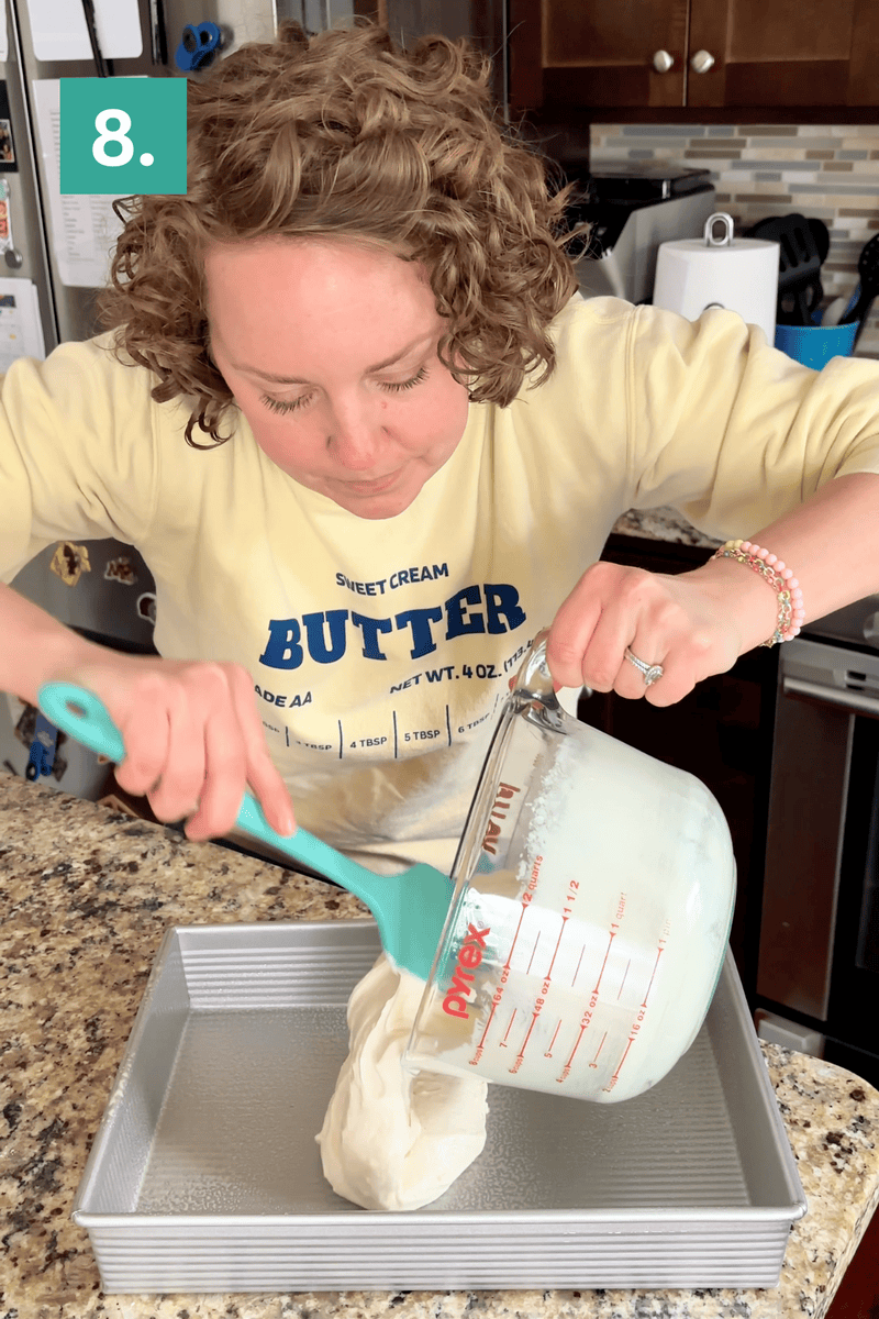 A woman pours a thick white batter from a glass measuring cup into a baking pan on a kitchen counter. She is wearing a yellow sweatshirt that says Sweet Cream BUTTER. A green box with the number 8 is in the top left corner.