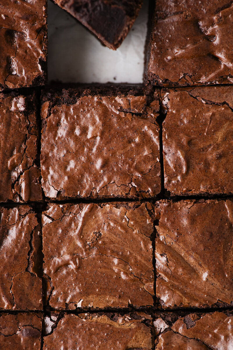 Close-up of fudgy, chocolate brownies cut into squares, with one brownie partially removed, revealing their shiny, crackly tops and rich, moist texture.