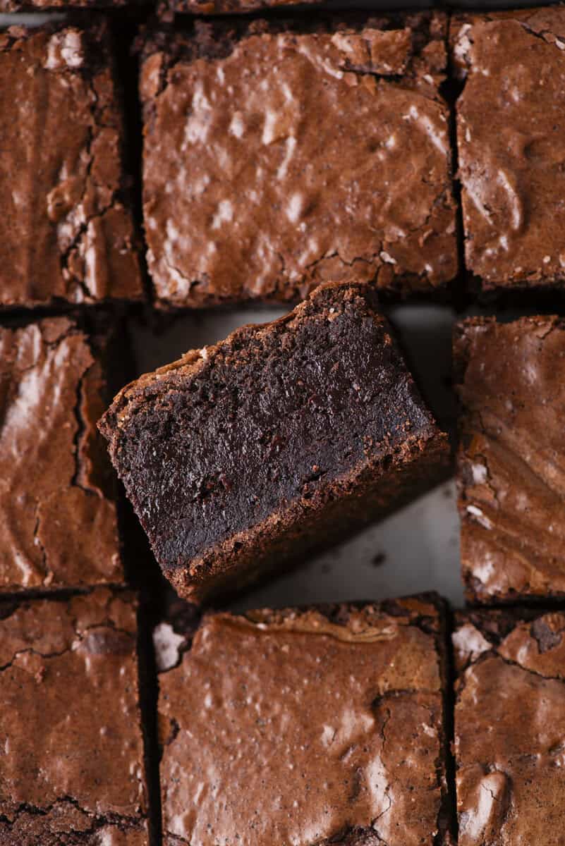 Close-up of sliced chocolate brownies, with one brownie turned on its side to show a rich, fudgy interior and a slightly crackled top.