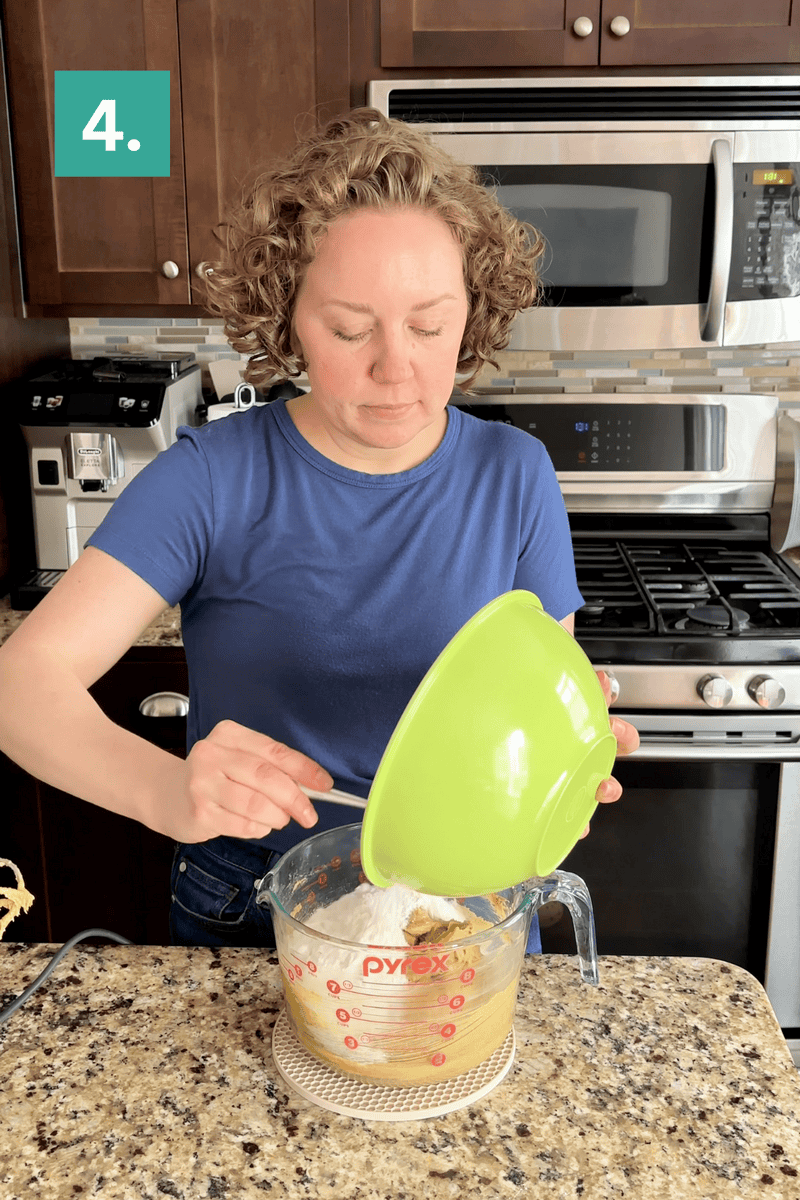A person in a blue shirt pours flour from a green bowl into a large Pyrex measuring cup on a kitchen counter. A step 4 label is in the top left corner. Stainless steel appliances are in the background.
