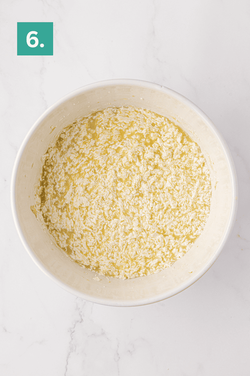 A white bowl filled with a mixture of wet and dry ingredients sits on a white marble surface. In the top left corner, a green box with the number 6 in white is visible.