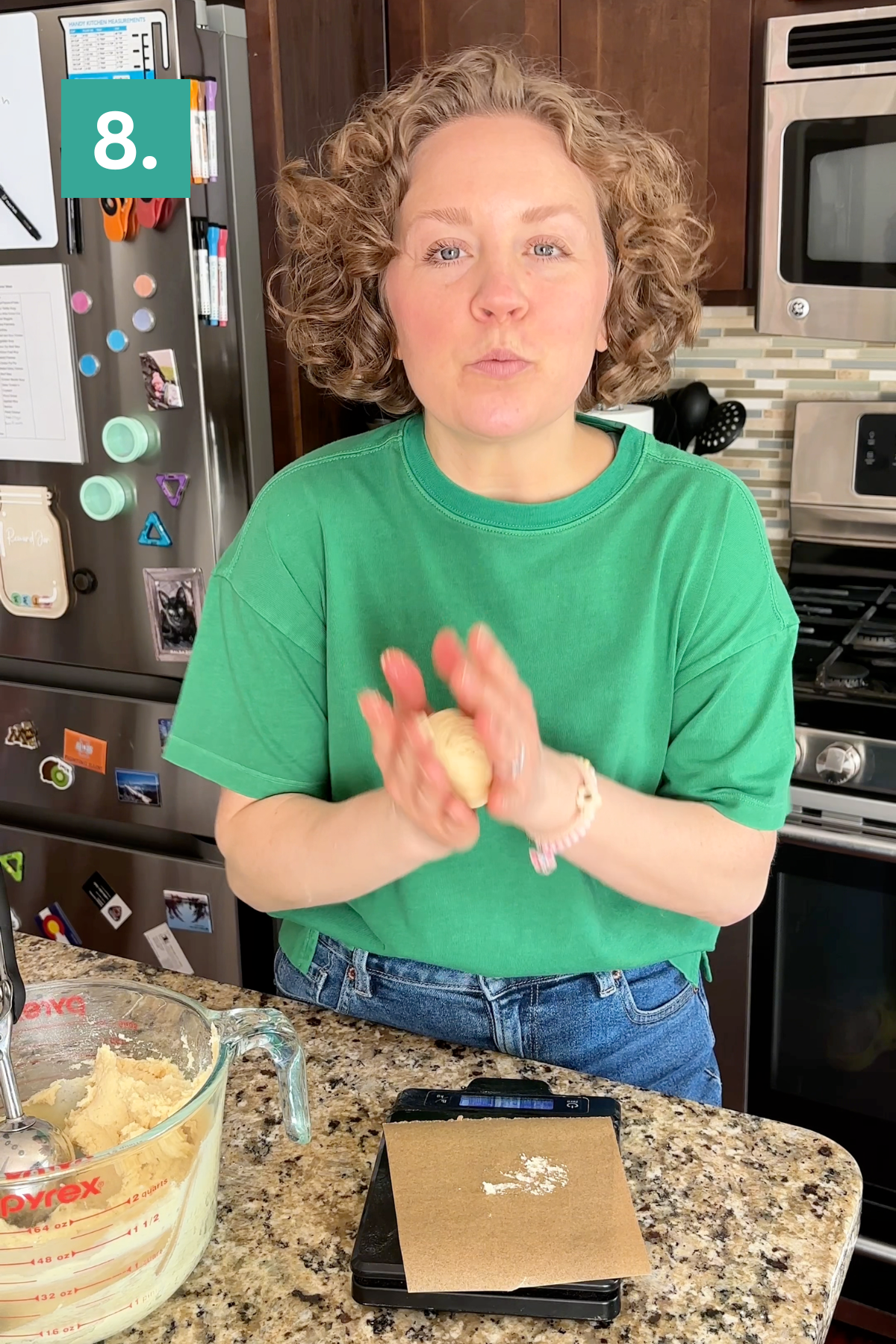 A woman in a green shirt stands in a kitchen, rolling dough with her hands over a digital scale on a granite counter. Baking ingredients and utensils are visible around her, and the number 8. appears in the top left corner.