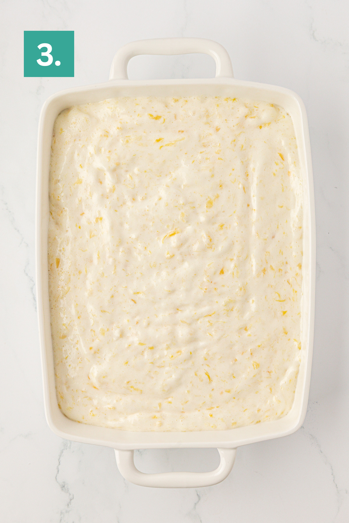 A white rectangular baking dish filled with a creamy, textured mixture sits on a white surface. A green square with the number 3 is in the top left corner of the image.