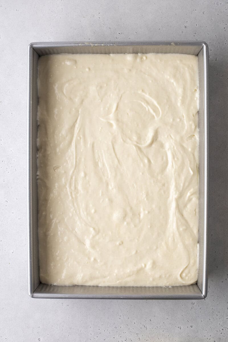 A rectangular metal baking pan filled with smooth, light-colored cake batter sits on a light gray surface, ready to be baked.
