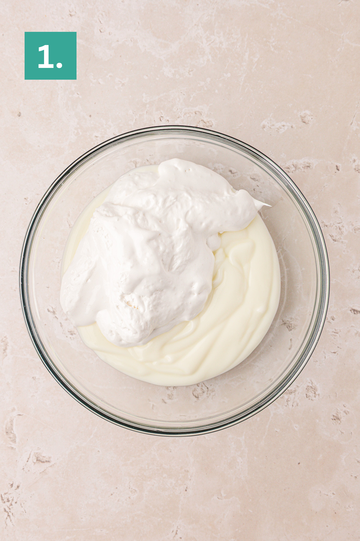 A glass bowl containing a mixture of thick white yogurt and whipped topping sits on a light beige surface. A green box with the number 1. appears in the top left corner.