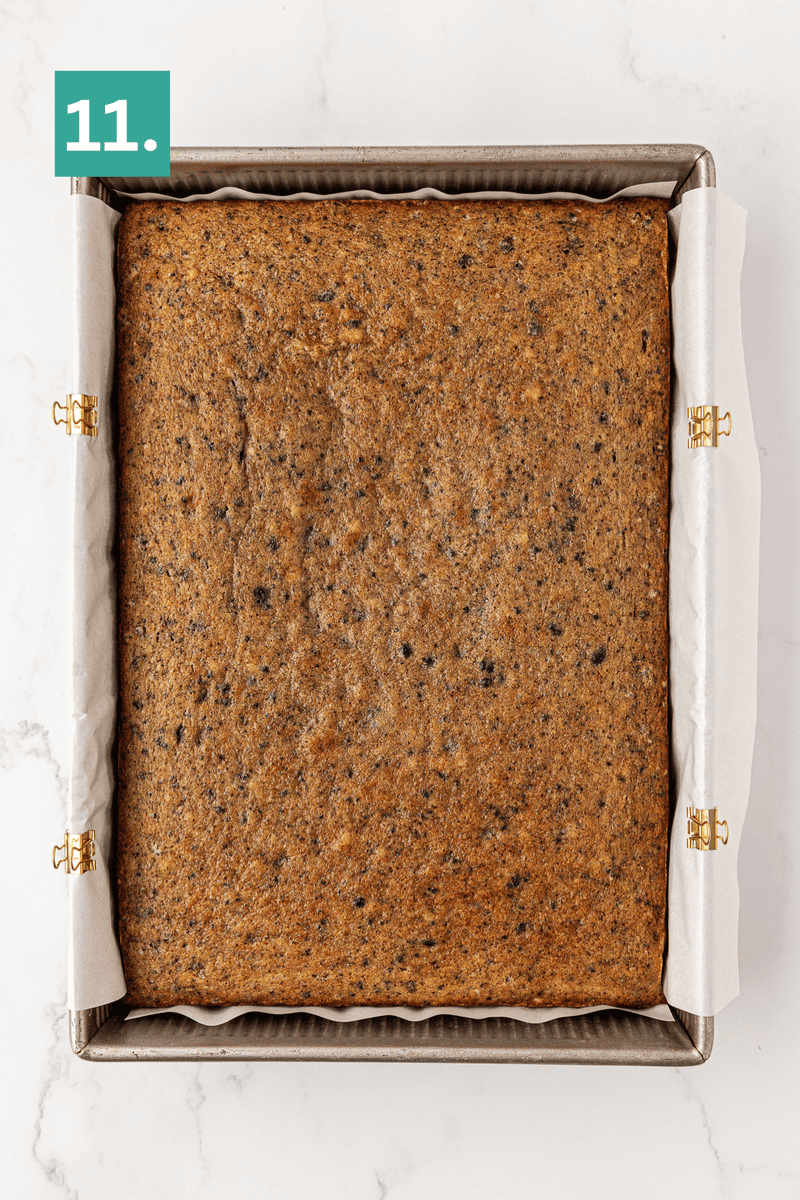 A square baking pan lined with parchment paper holds a golden-brown, baked cake. The number 11. appears in a green box in the top left corner of the image.