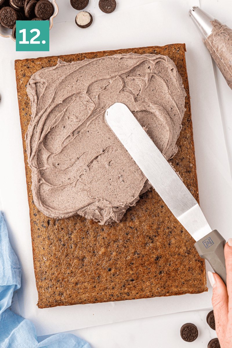 A rectangular cake is being frosted with chocolate icing using a spatula. Small cookies and a piping bag are nearby. A green box with the number 12 is in the top left corner.