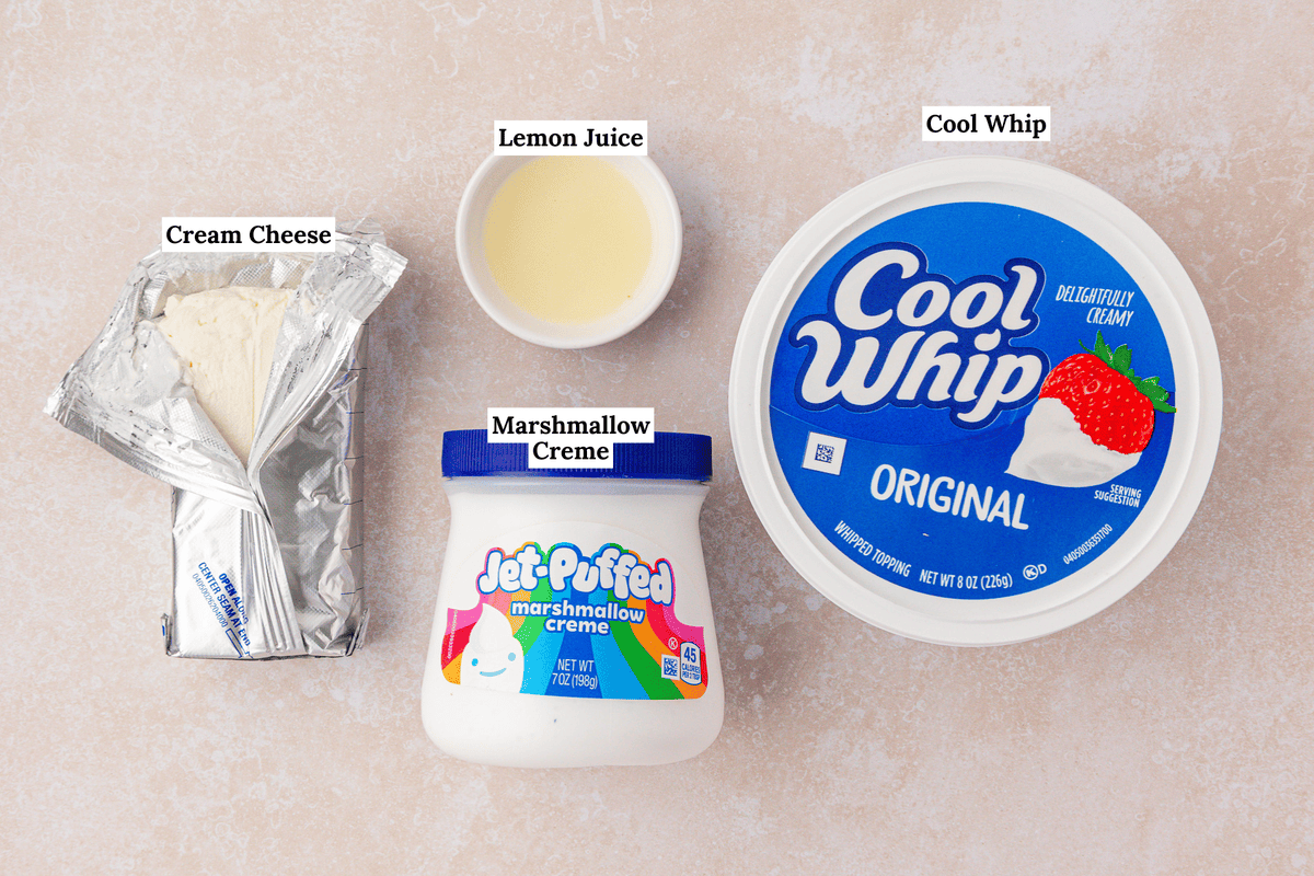 Four ingredients on a countertop: an unwrapped block of cream cheese, a small bowl of lemon juice, a jar of marshmallow creme, and a large tub of Cool Whip. Each item is labeled.