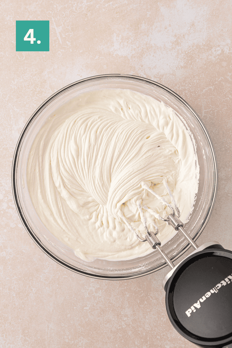 A glass bowl filled with whipped cream and an electric hand mixer on the side. A green box with the number 4 is in the upper left corner.