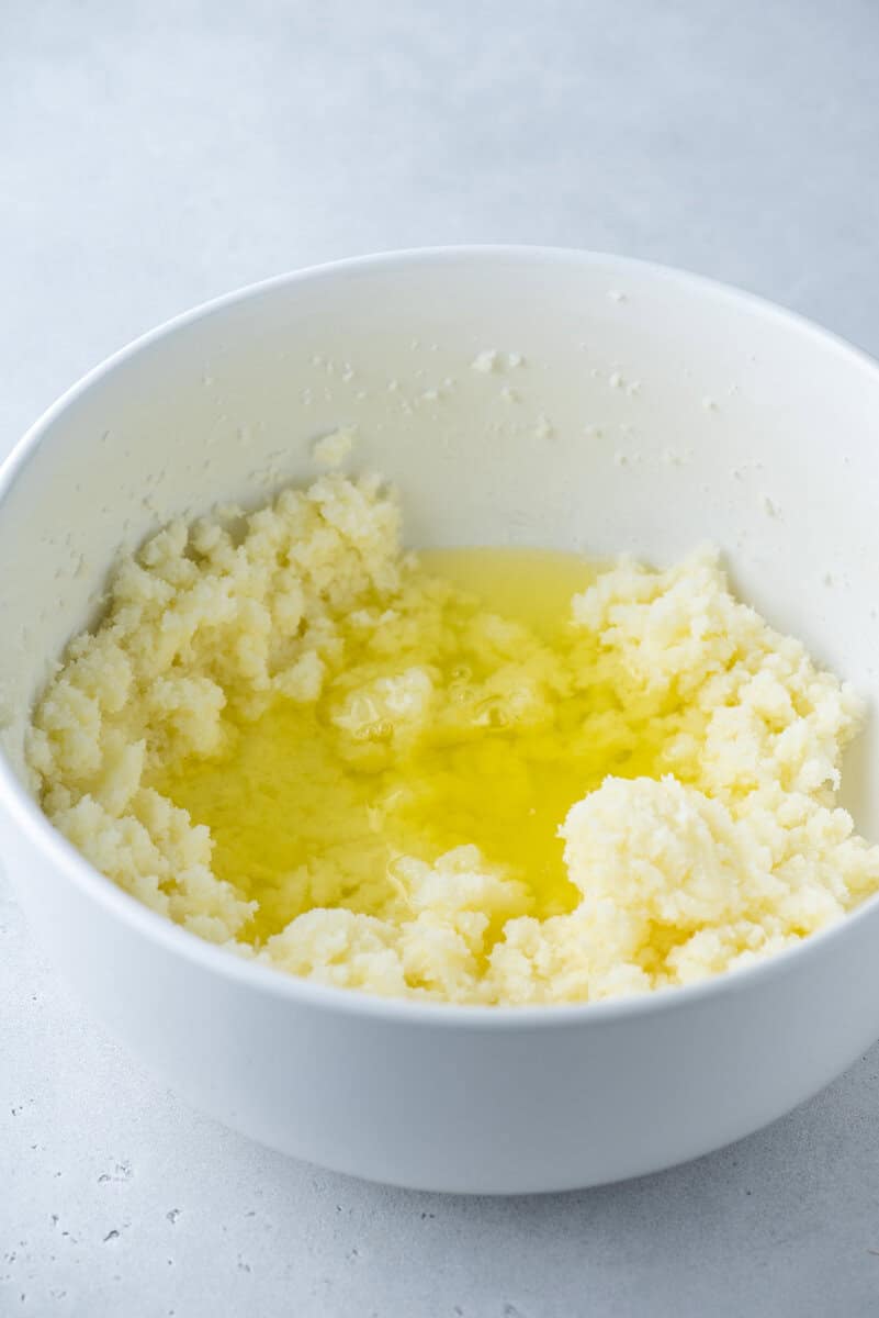 A white mixing bowl containing creamed butter and sugar with melted butter pooled in the center, set on a light-colored countertop.