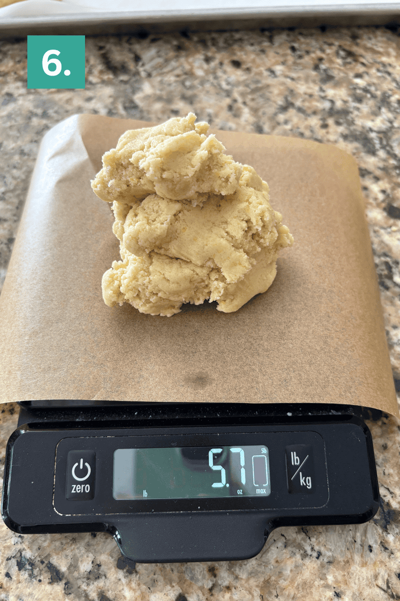 A digital kitchen scale displays 57 grams with a mound of cookie dough on parchment paper, placed on a granite countertop. A green box with the number 6 is in the top left corner.