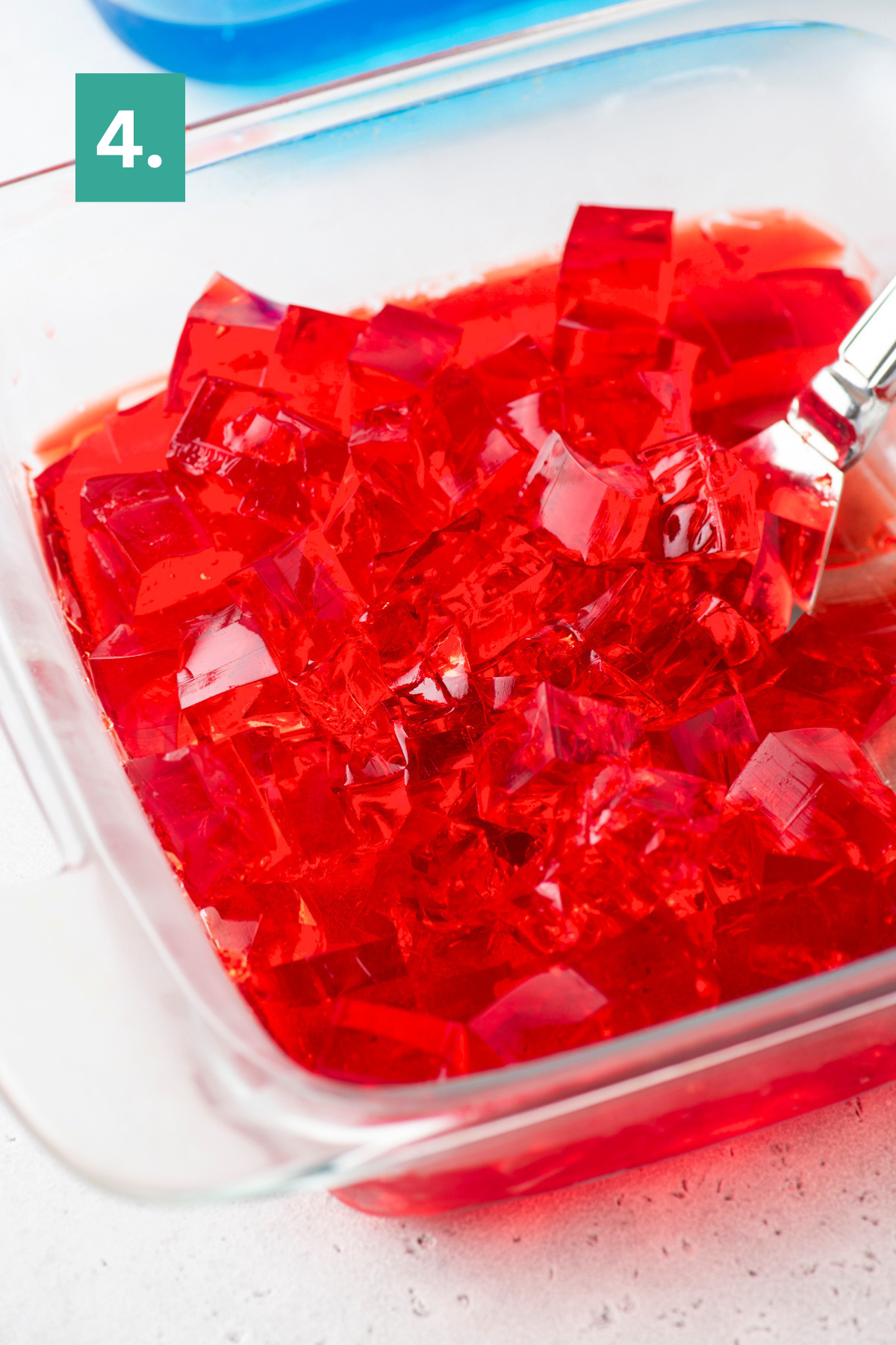 A glass dish filled with red gelatin cut into cubes, with a serving spoon inside. A green box with the number 4 is in the top left corner.