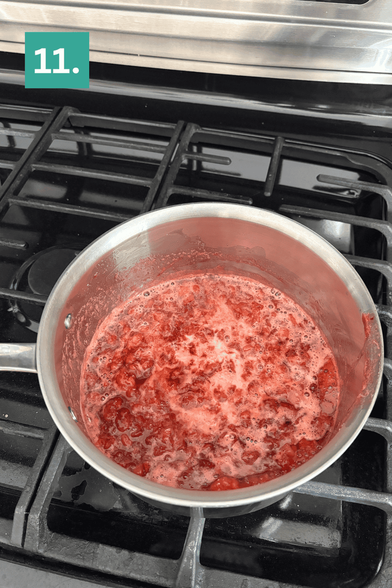 A saucepan with bubbling, mashed red fruit mixture is on a stove. A green box with the number 11 is in the top left corner, indicating a recipe step.