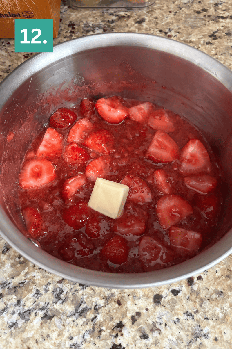 A metal pot contains sliced strawberries in a red sauce with a pat of butter melting on top. The pot sits on a granite countertop, and a green box with the number 12 is in the top left corner.