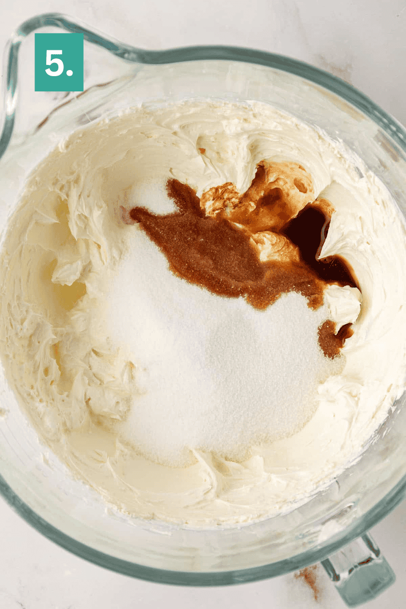 A glass mixing bowl with whipped cream cheese, granulated sugar, and vanilla extract, ready to be mixed. A green square with the number 5 is in the top left corner.