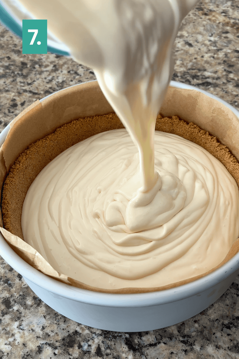 A creamy cheesecake filling is being poured into a round pan lined with parchment paper and a graham cracker crust. A green box in the top left corner displays the number 7.