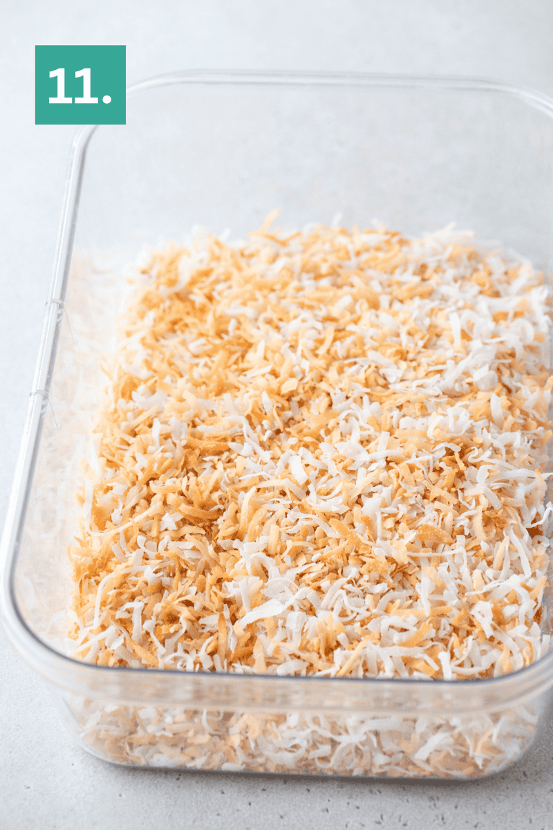 Glass container filled with toasted shredded coconut, some pieces golden brown and others white. A green box in the top left corner displays the number 11. The background is a light, smooth surface.