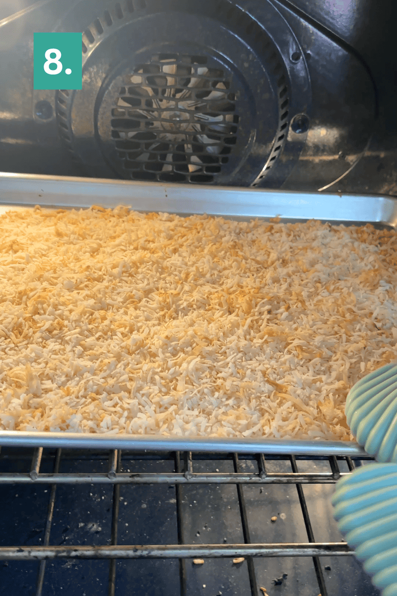 A hand in an oven mitt pulls a baking sheet with toasted shredded coconut from an oven. A green square with the number 8 is in the top left corner.