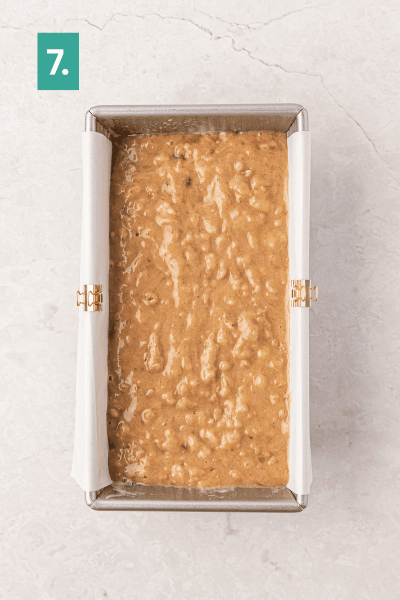 A metal loaf pan lined with parchment paper is filled with banana bread batter. A green box with the number 7 is in the upper left corner of the image.