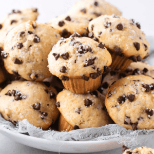 A plate filled with mini chocolate chip muffins topped with sugar crystals, arranged on a light cloth.