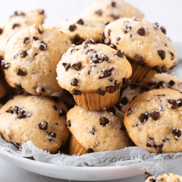 A plate filled with mini chocolate chip muffins topped with sugar crystals, arranged on a light cloth.