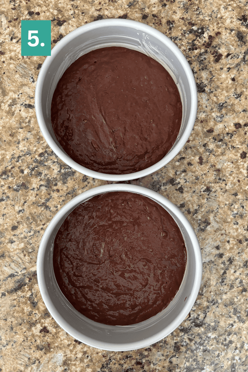 Two round cake pans filled with chocolate batter are placed on a speckled countertop. A green box in the top left corner displays the number 5 in white.