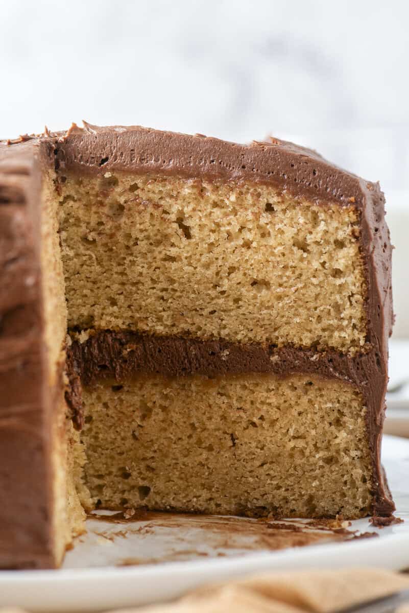 A close-up of a sliced yellow cake with two layers, filled and topped with chocolate frosting, on a white plate.