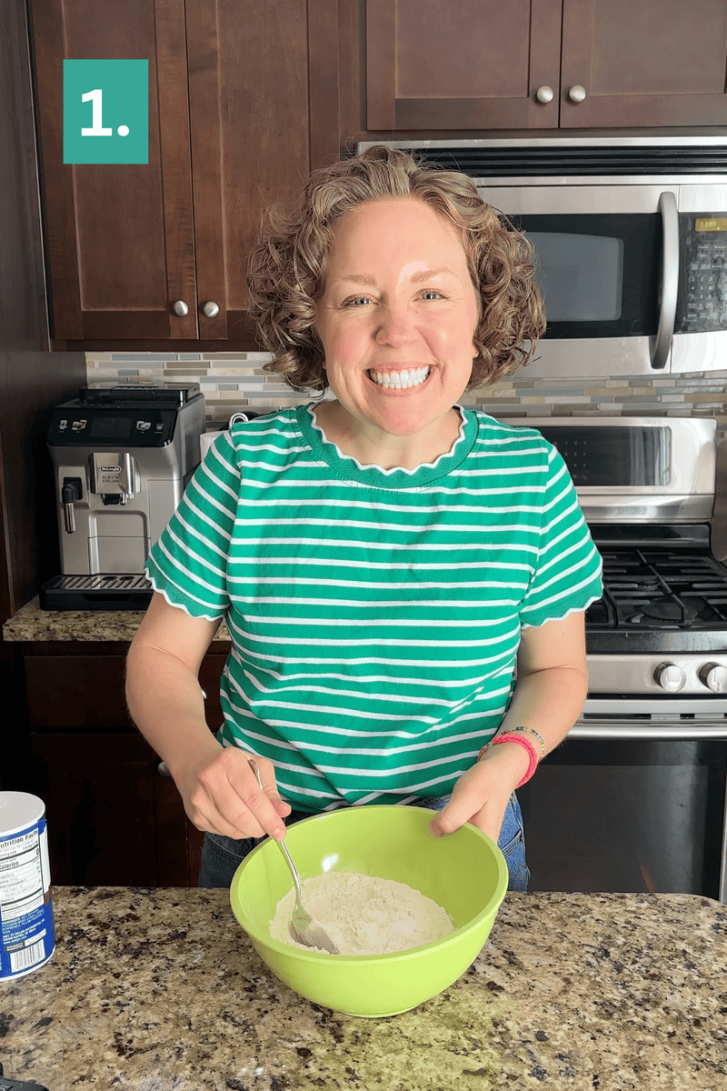 Smiling person in a green striped shirt mixes flour in a green bowl on a kitchen counter. A microwave, oven, and coffee machine are visible in the background. A “1.” appears in the top left corner.