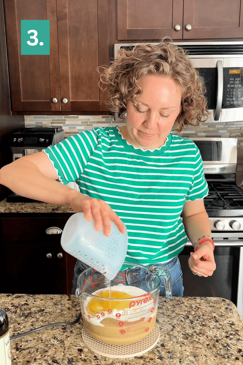A woman in a green striped shirt pours liquid from a measuring cup into a Pyrex bowl with eggs and sugar on a kitchen counter. A green box with a white 3. appears in the upper left corner.