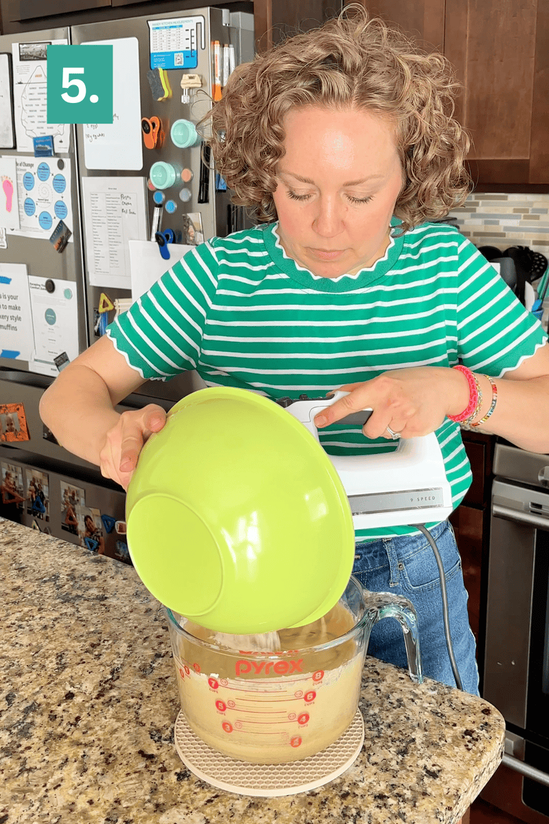 A woman in a green striped shirt pours batter from a green bowl into a glass measuring cup on a kitchen counter, holding a hand mixer. A 5. label is in the top left corner.