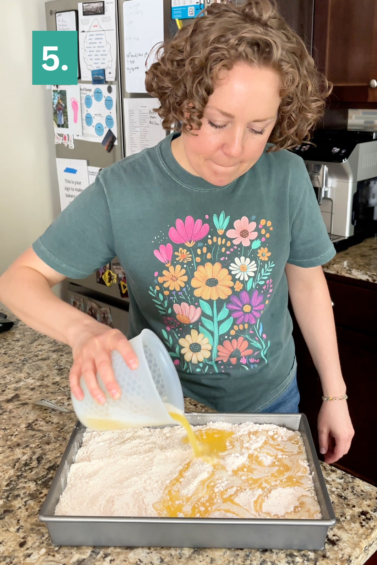 A person in a floral shirt pours a liquid mixture into a pan of flour on a kitchen counter, preparing what looks like the base for a Strawberry Cheesecake Dump Cake. A green box labeled 5. appears in the top left corner.