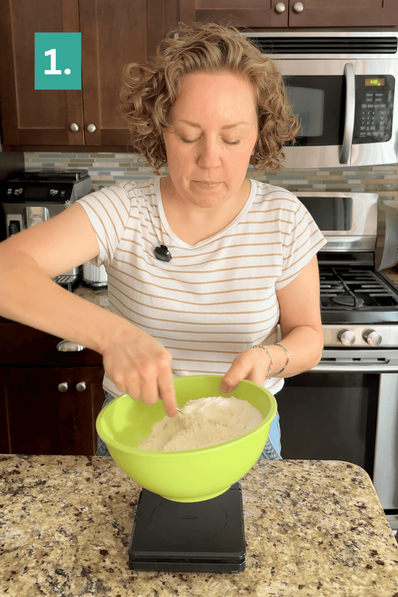 A woman stands in a kitchen, mixing flour in a green bowl on a digital scale. She wears a striped shirt and has curly hair. There is a 1. label in the top left corner of the image.