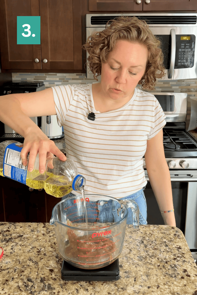 A person in a striped shirt pours oil from a bottle into a clear measuring cup on a kitchen counter. A green box with 3. is in the upper left corner. Kitchen appliances are visible in the background.