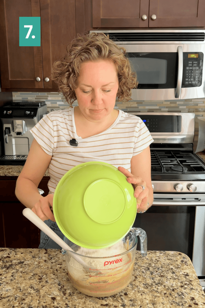 A woman in a striped shirt pours flour from a green bowl into a glass measuring cup on a kitchen counter. A number 7 is in the top left corner.