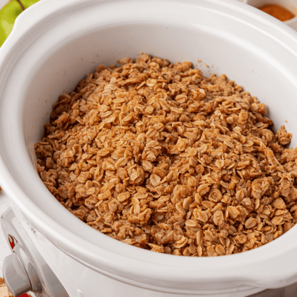 A white slow cooker filled with golden brown granola made of oats and spices.