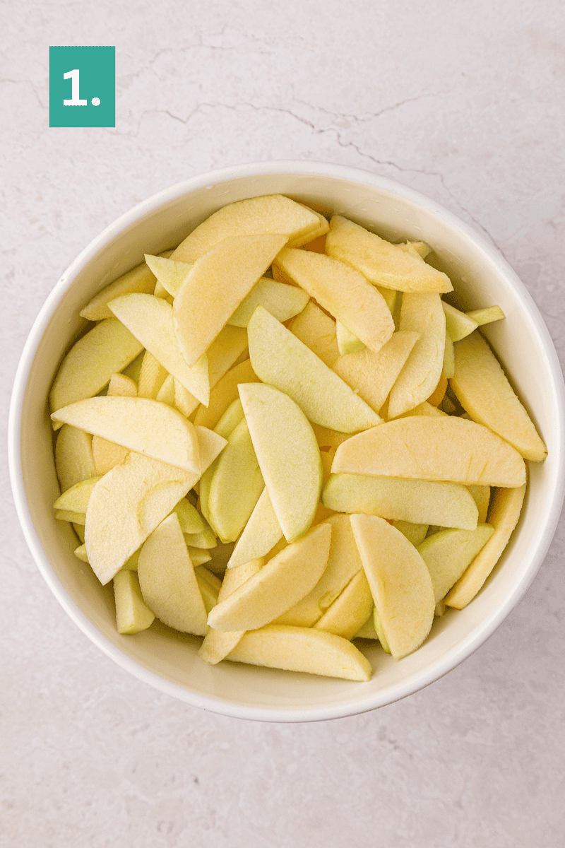 Bowl filled with peeled and sliced apples on a light countertop, with a green box labeled 1 in the upper left corner.