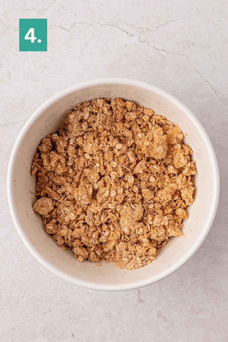 A white bowl filled with oat crumble mixture sits on a light countertop. A green square in the top left corner displays the number 4 with a period.