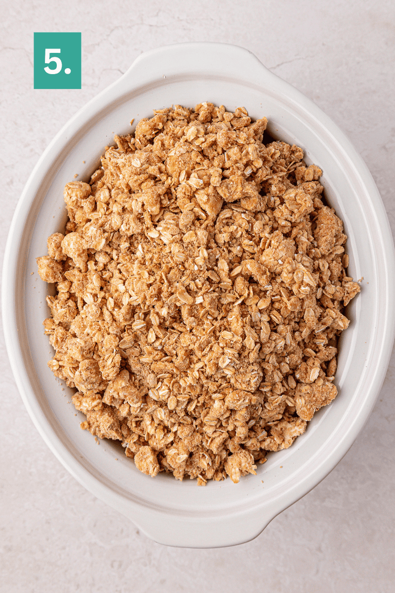 Oval white dish filled with an oat and crumb topping sits on a light surface. A green box with the number 5 is in the top left corner.