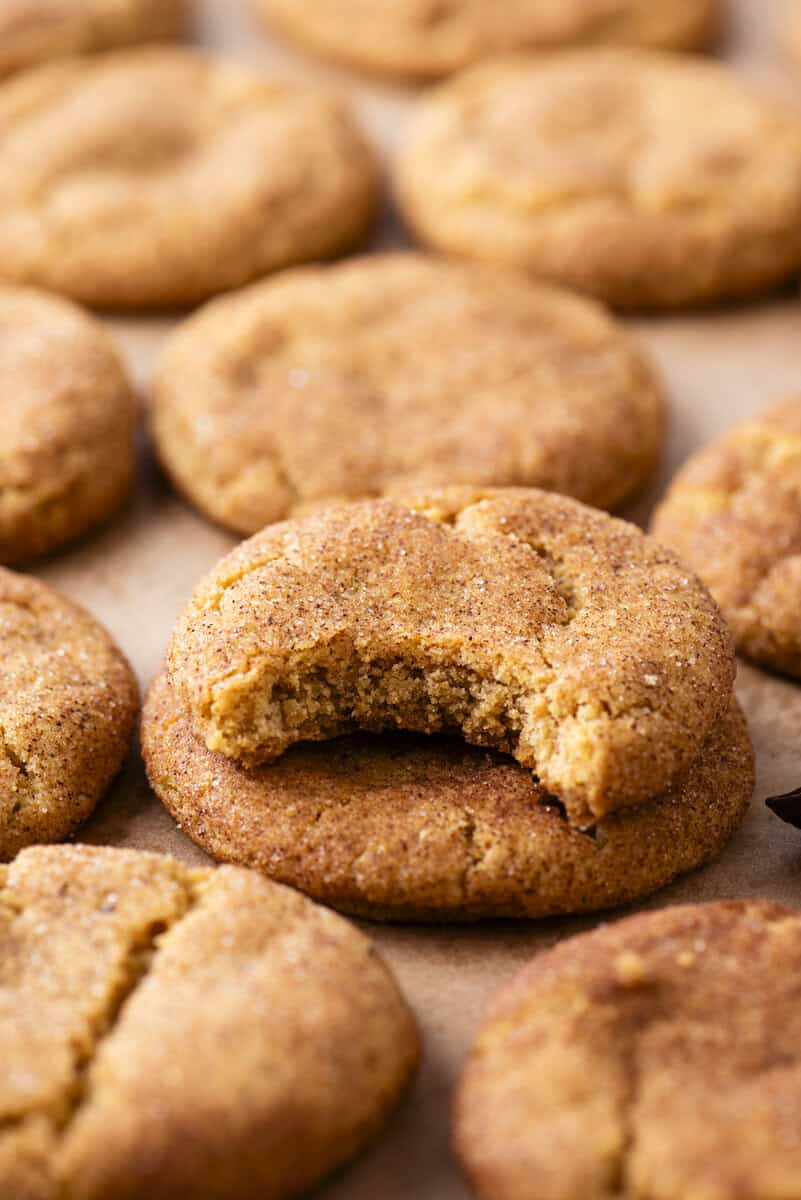 A close-up of several snickerdoodle cookies on parchment paper, with one cookie in the center showing a bite taken out of it.