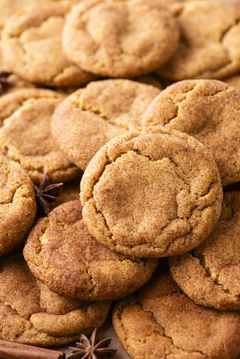 A close-up of several golden-brown snickerdoodle cookies stacked together, showing their cracked, cinnamon-sugar coated surfaces.