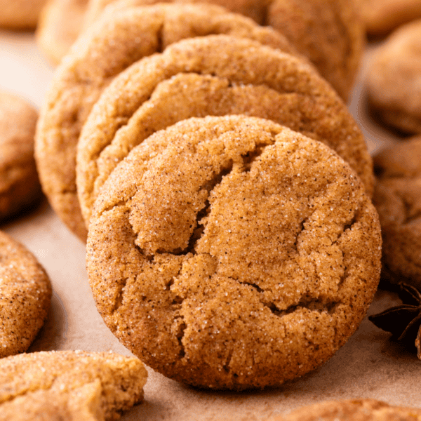 Close-up of several golden-brown snickerdoodle cookies with a crackled surface, coated in cinnamon sugar, arranged on a parchment-lined surface.